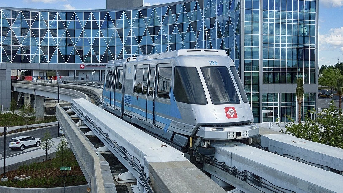 A Skyway train moving on a monorail, with the JTA headquarters in the background.