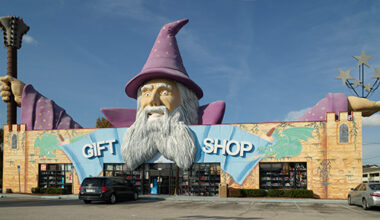Large building that is designed to look like a castle that says Gift Shop on the front above the doors. Above the building is a large wizard with a purple had and cloaks holding up a staff.