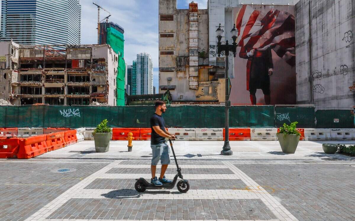 An electric scooter travels on a paved Flagler Street as sidewalks are blocked as demolition of Mana Properties buildings on 48 E. Flagler Street continues in downtown Miami on Tuesday, August 4, 2026.