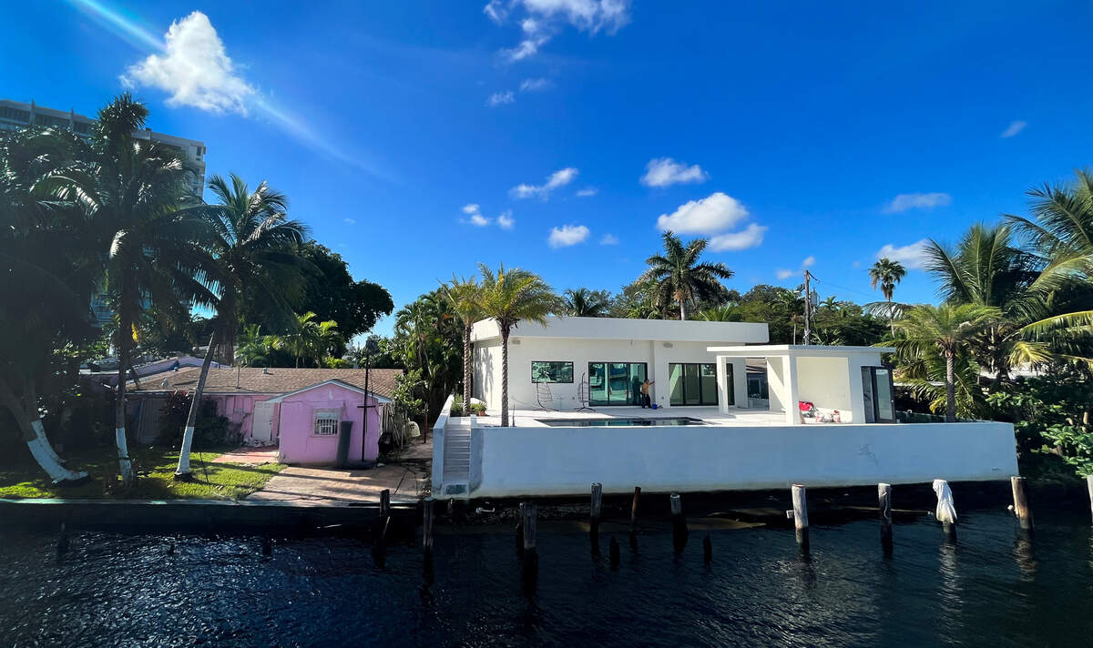 Two next-door homes along the Miami River show the impact of new building and elevation standards compared to older stock housing. Both homes are only one story, but the newer house appears nearly twice as tall as the older one.