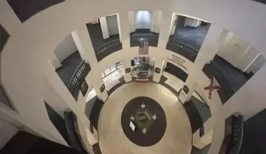 A view looking down through the open rotunda of the Leon County Courthouse in Tallahassee. On the ground floor, the county seal is embedded in the tile floor beneath an American flag hanging from the second level.