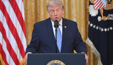 Donald Trump speaking at a podium bearing the seal of the President of the United States, flanked by the American flag and the Presidential flag.