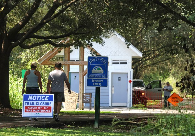 Signage indicates a closed trail as Seminole County workers repair drainage on the Cross Seminole Trail at the Black Hammock Trailhead, off State Road 434 at S.R. 417, Wednesday, August 12, 2026. Residents worry that the 46-acre wooded greenbelt known as Jetta Point adjacent to the trail will be sold off to developers by Seminole County, possibly worsening ongoing flooding concerns in the area. (Joe Burbank/Orlando Sentinel)