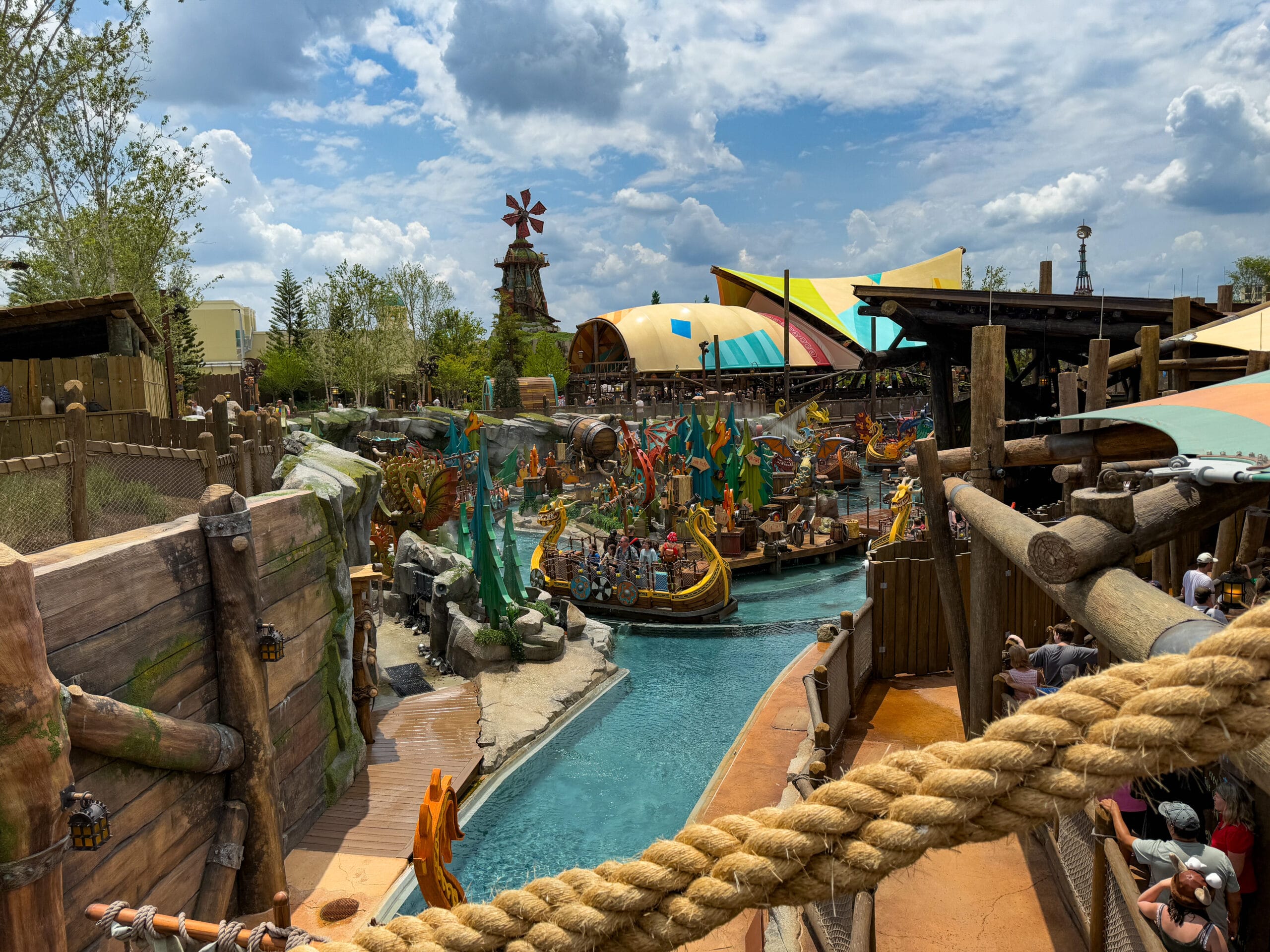 Colorful theme park water ride with Viking boats in Epic Universe, surrounded by lush scenery and a partly cloudy sky.