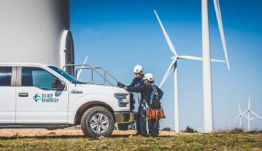 Two Duke Energy technicians stand beside a company truck and wind turbines.