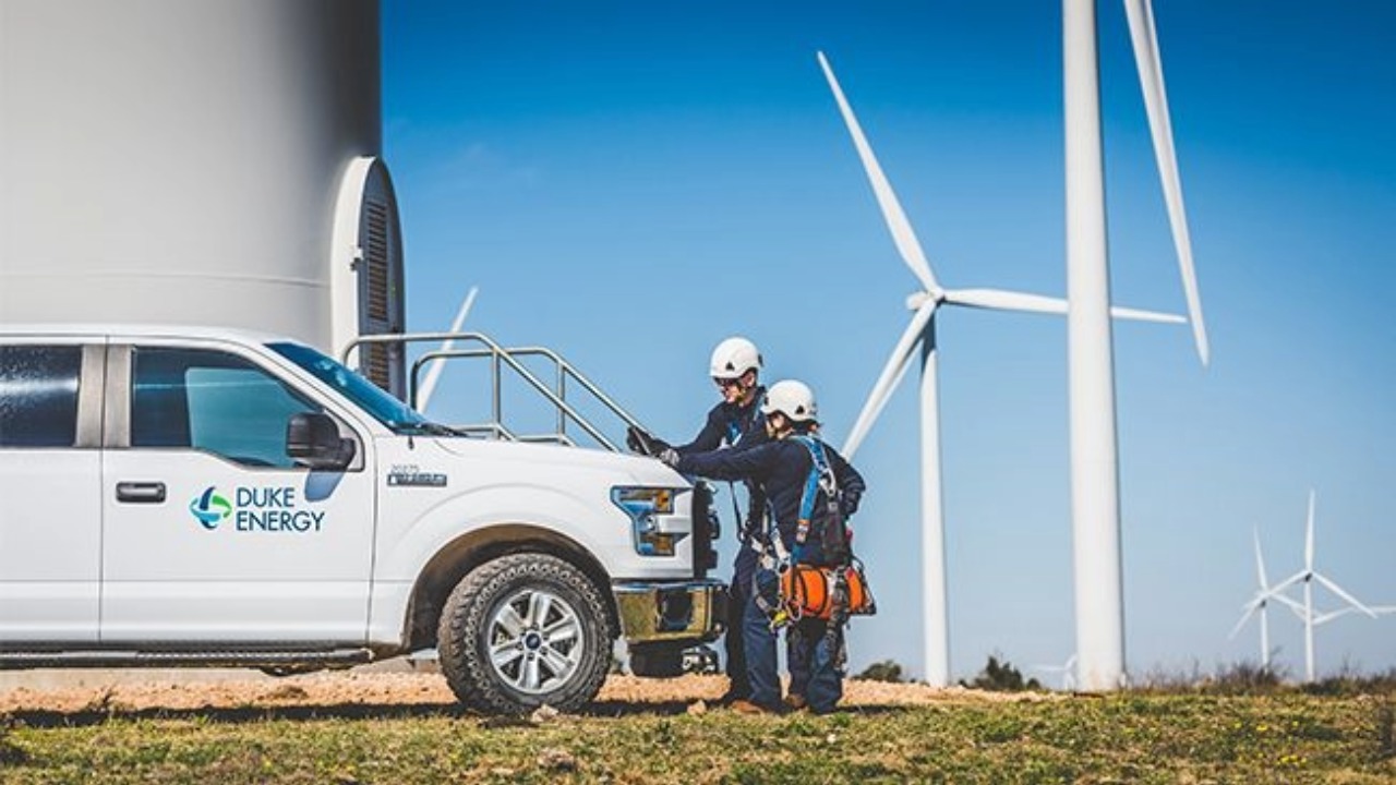 Two Duke Energy technicians stand beside a company truck and wind turbines.