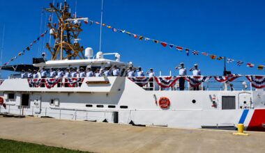 Coast Guard crew members stand aboard a cutter decorated with signal flags and patriotic bunting.