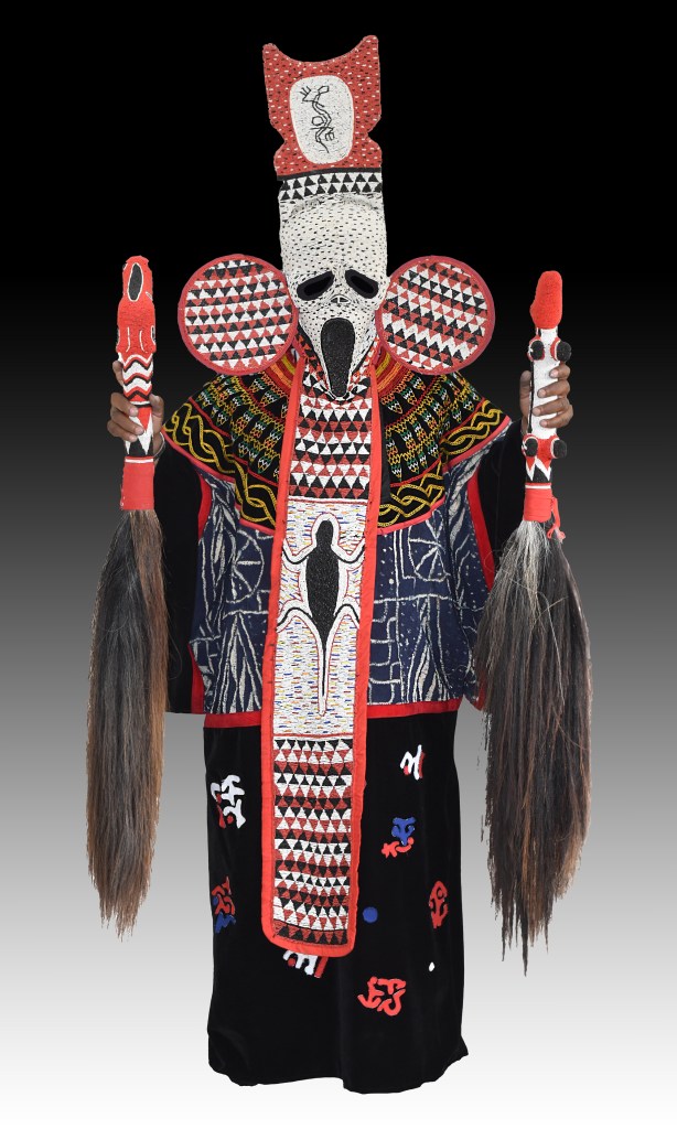 A studio photograph of the full-length Tso Scream Mask ensemble from the Visages de masques (IX) series (2015–23) by artist Hervé Youmbi, in the collection of the New Orleans Museum of Art. Displayed center frame against a gradient background transitioning from black to white, the intricate masquerade outfit features a beaded white face mask resembling the iconic Scream mask with dark hollow eyes, an open mouth, large circular ear discs, and a tall red-and-white crown structure. A long central front panel covered in white, black, and red geometric beadwork extends down the torso over a dark blue patterned tunic and a black velvet skirt decorated with colorful embroidered symbols. Hands wearing long, dark horsehair flywhisks hold tall beaded staves on either side of the figure.