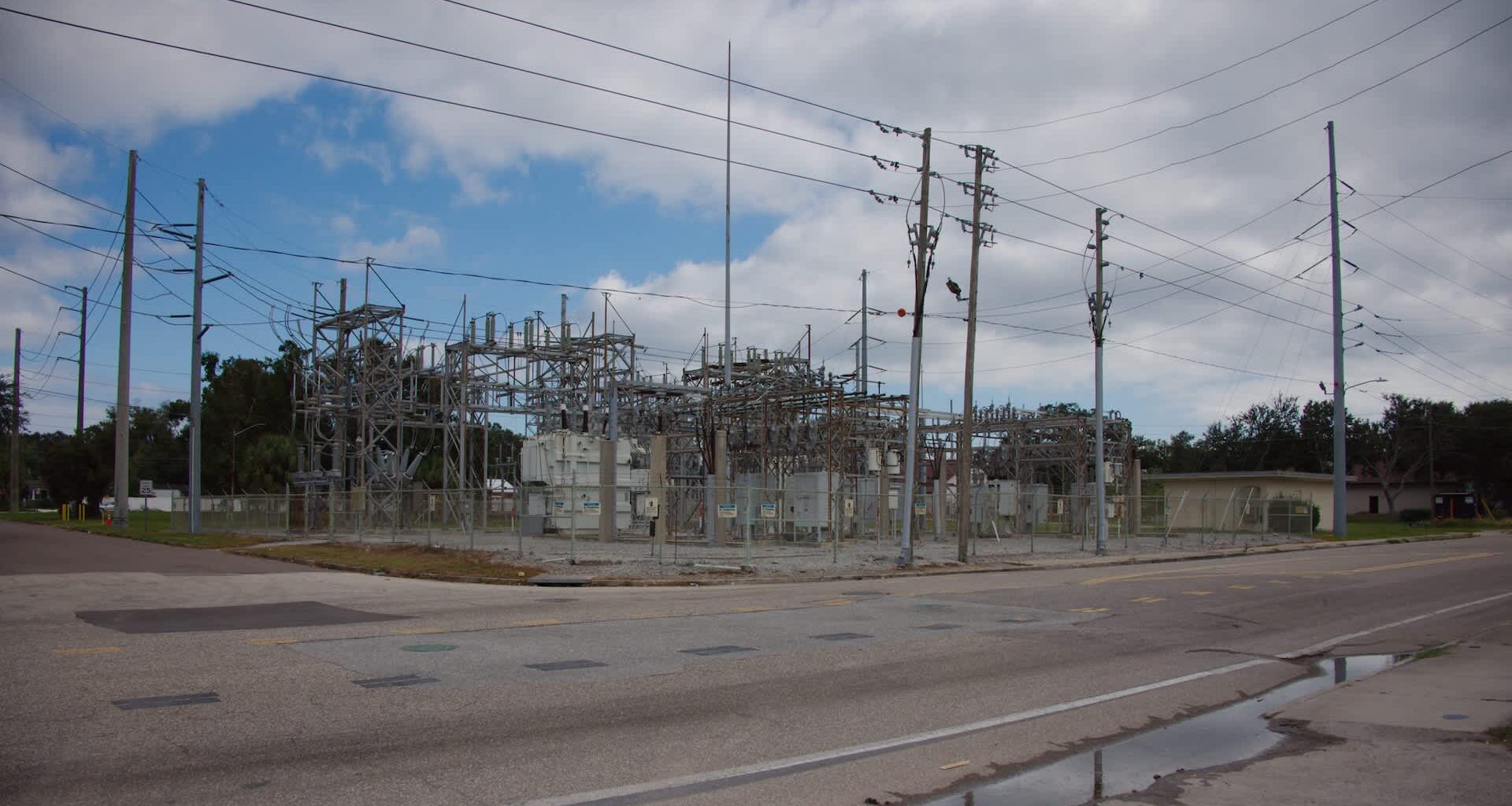 An electrical substation with towers, power lines, and a fenced area next to a road.