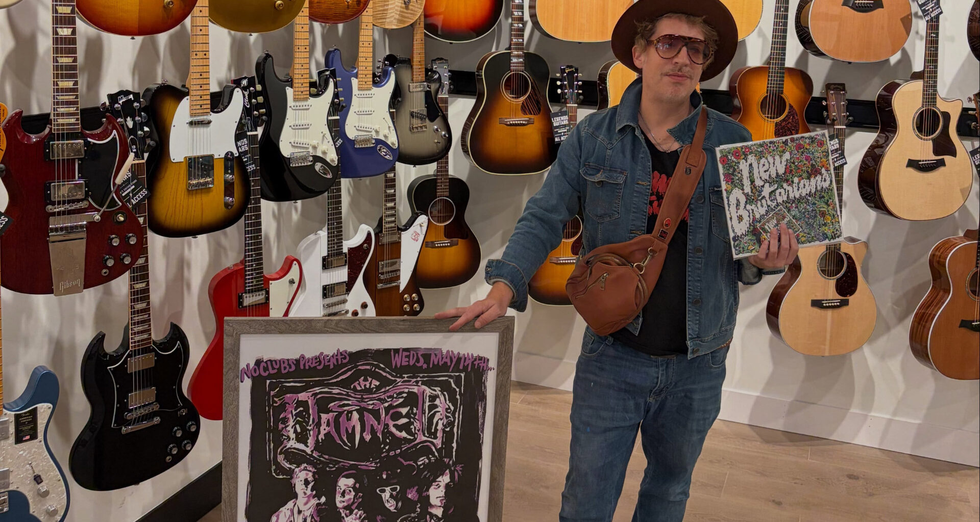 man showing off music and art in front of a wall of guitars