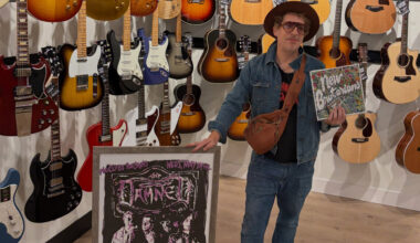 man showing off music and art in front of a wall of guitars