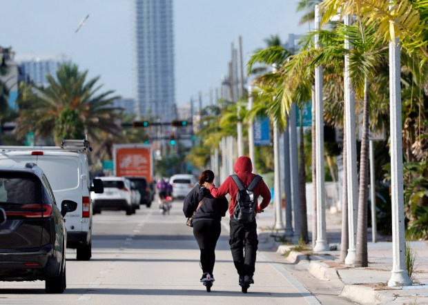 A couple rides e-scooters down Ocean Drive in Hollywood on Friday, a tall tower looming in the distance. More tall towers could be on the way if the city relaxes its current height cap at the beach. (Amy Beth Bennett/South Florida Sun Sentinel)