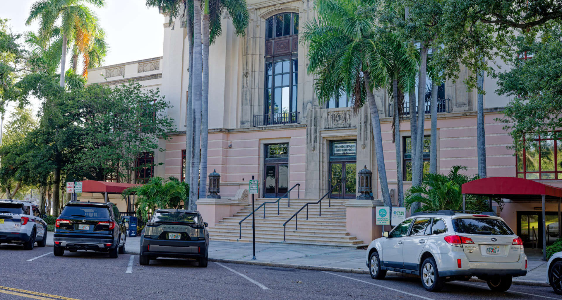 A historic building with palm trees and parked cars in front.