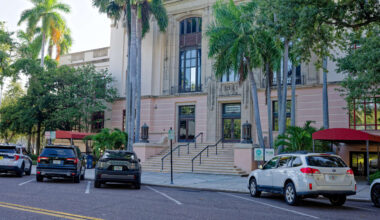 A historic building with palm trees and parked cars in front.