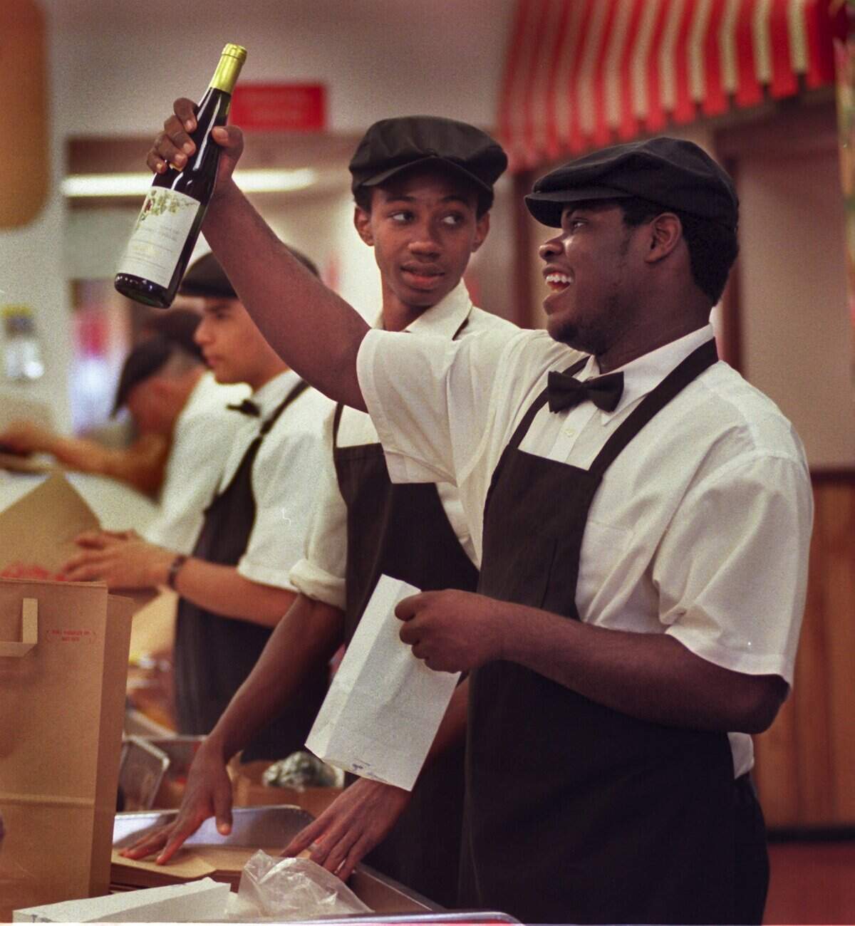 In 1999, Epicure Market employee Billy Belony, right, teases a customer at checkout as he bags several bottles of champagne and wine for New year’s.