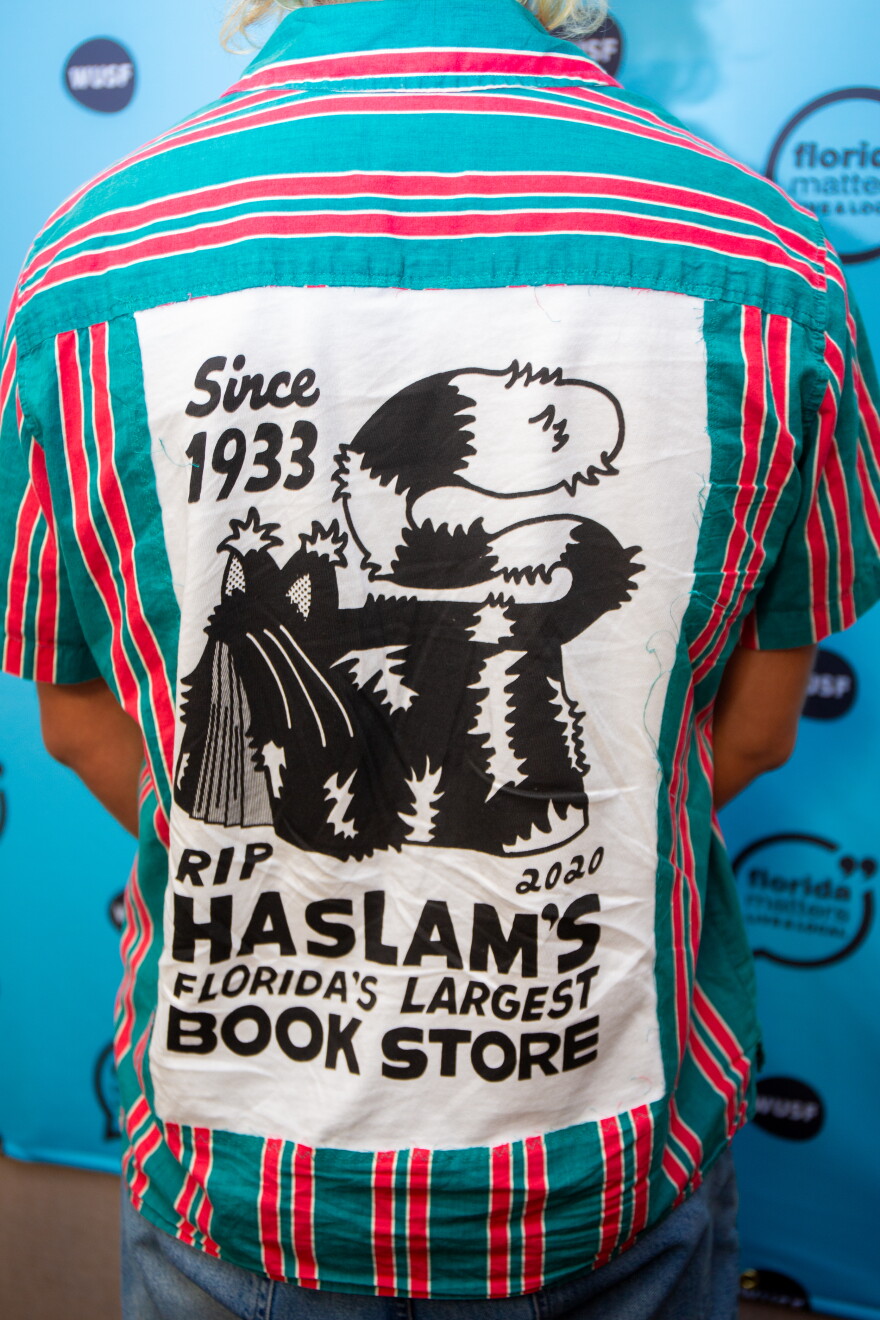 The back of a blue and red striped shirt with a large t-shirt patch sewn to it. It’s white with black text that says RIP Haslam’s Florida’s LArgest Book Store 2020 Since 1993” with an illustration of a cat.