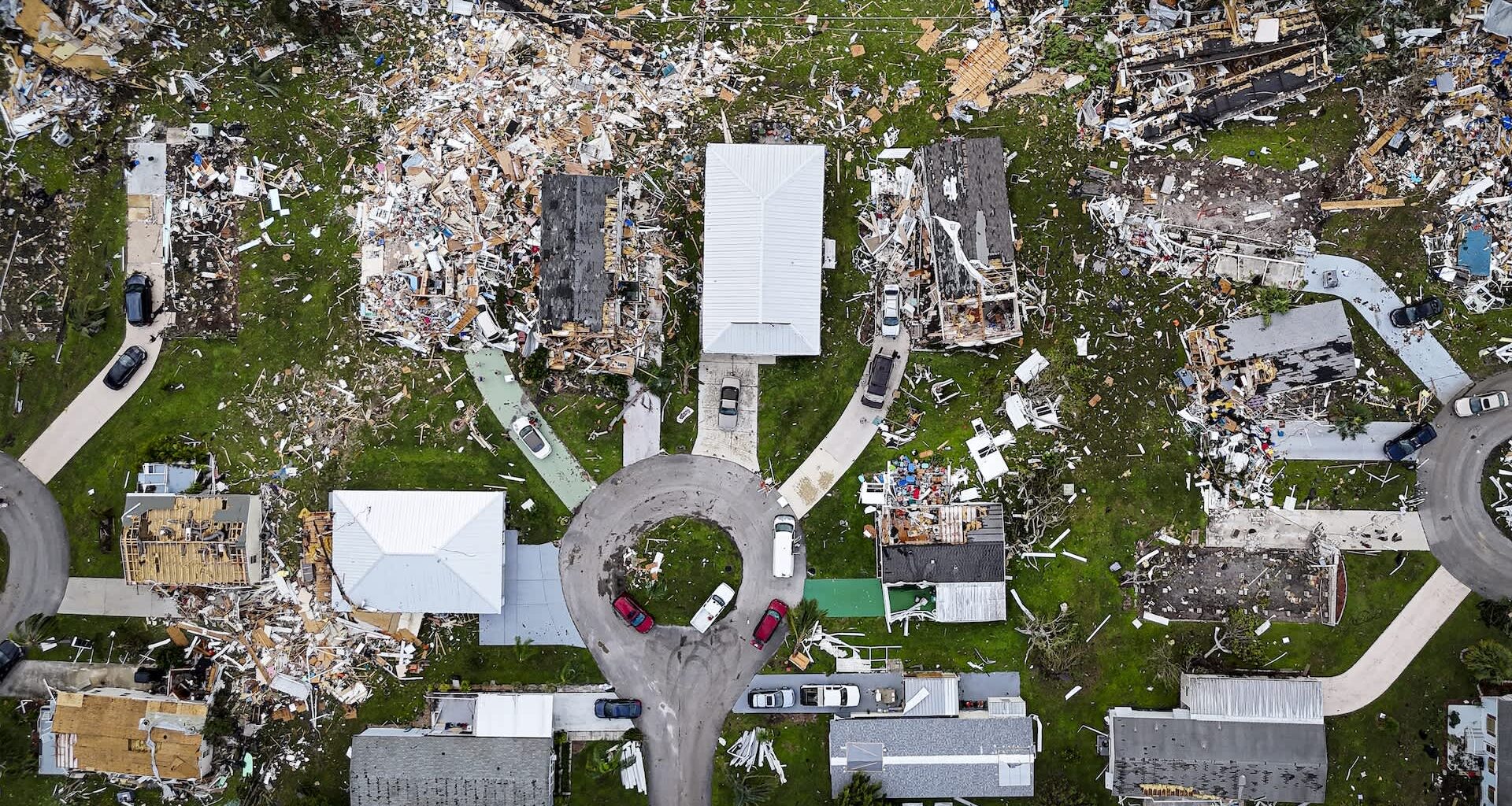 An aerial view of a neighborhood showing damaged homes and debris scattered across the ground.