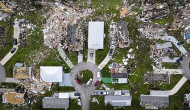 An aerial view of a neighborhood showing damaged homes and debris scattered across the ground.