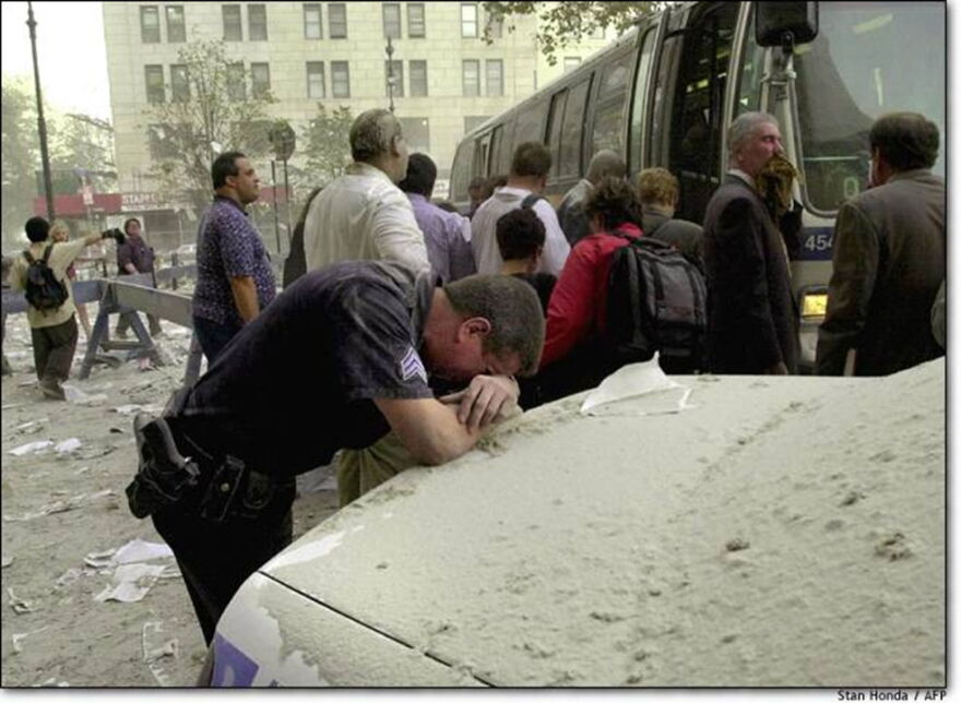 NYPD officer breaks down in tears on trunk of police cruiser covered with thick layer of soot.