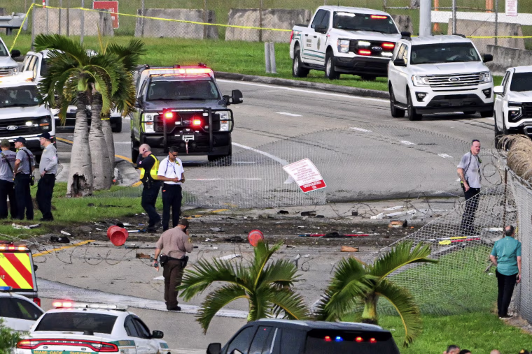 Rescue personnel stand amidst debris and wreckage following an accident.