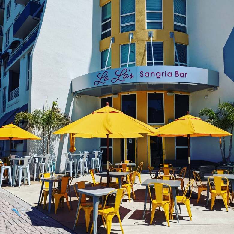 Exterior view of La La's Sangria Bar featuring yellow patio umbrellas and vibrant yellow and blue architecture.