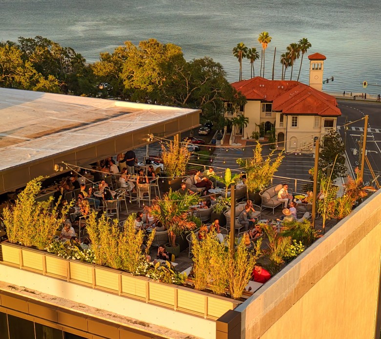 Rooftop lounge at O-Ku Tampa overlooking trees, waterfront views, and surrounding architecture at sunset.