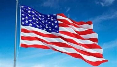 An American flag waving in the wind with a clear blue sky surrounding it.