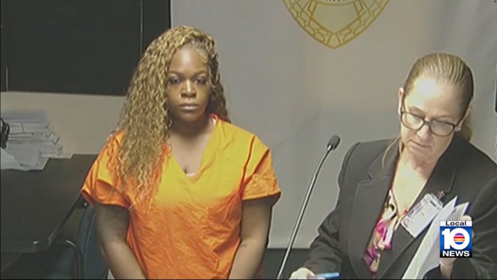 Nathalie Belizaire, accused of child neglect, stands in an orange jumpsuit before Judge Mindy Glazer in a courtroom.