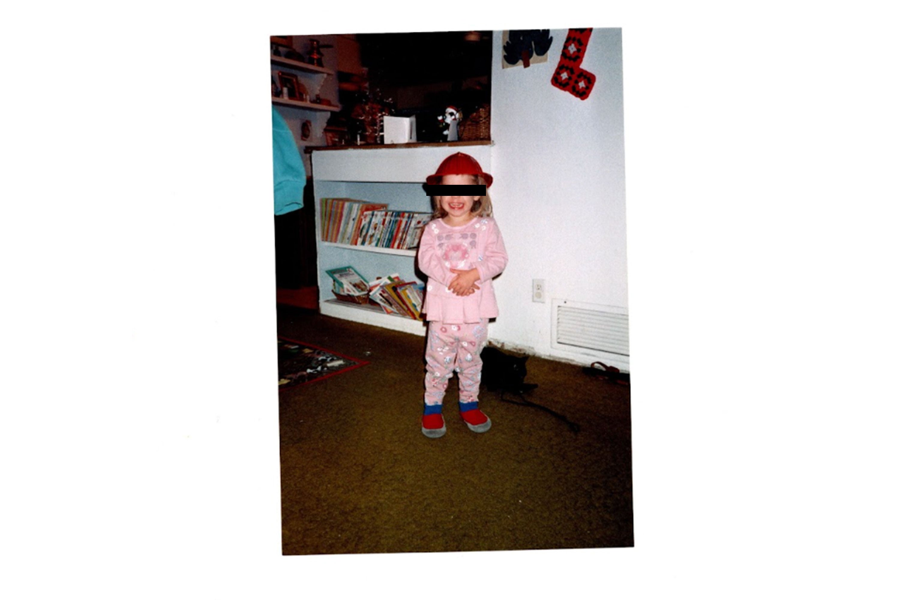 A toddler dressed in pink, smiling, with her eyes Sharpied out.