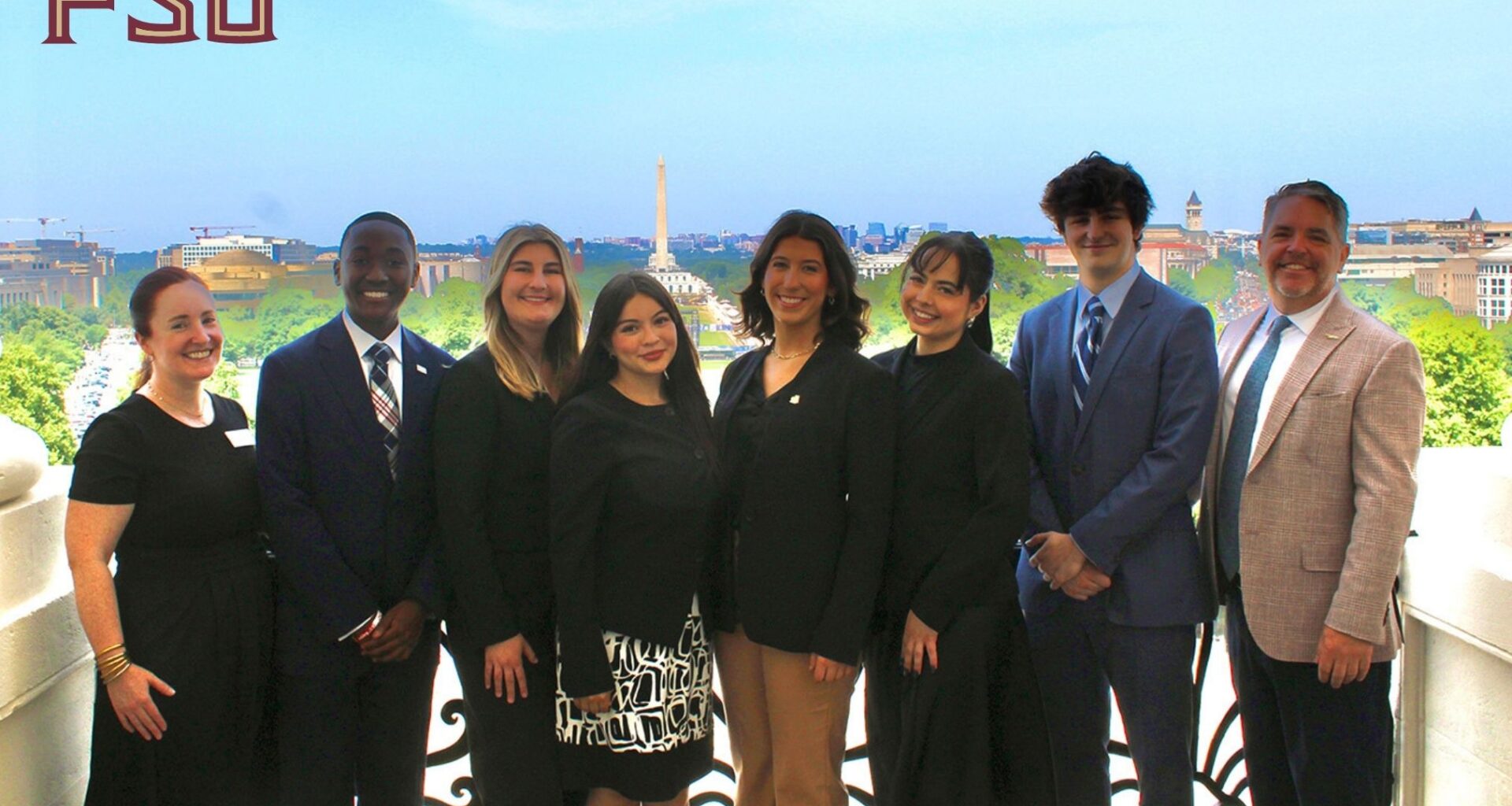 Eight people pose for a photo in professional clothing on a balcony overlooking the national mall in Washington, D.C.