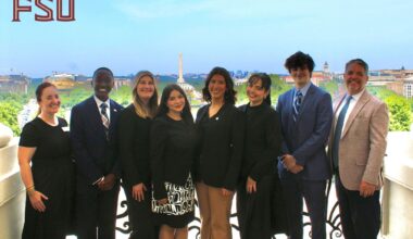 Eight people pose for a photo in professional clothing on a balcony overlooking the national mall in Washington, D.C.