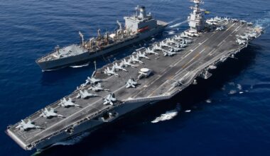 U.S. Navy aircraft carrier underway at sea alongside a replenishment ship, with aircraft positioned across the flight deck.