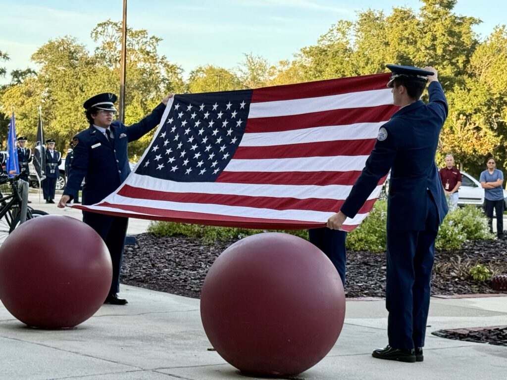 Cadets Rodosvaldo Munoz III (left) and Anthony Darwin (right) display the flag presented to Maria Vazquez before beginning the 13 folds.