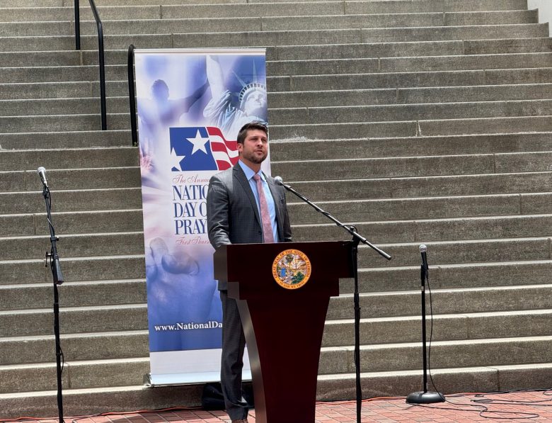 James Uthmeier, Chief of Staff to Governor Ron DeSantis, speaking at a microphone during the Annual National Day of Prayer event in front of the Florida State Capitol steps.