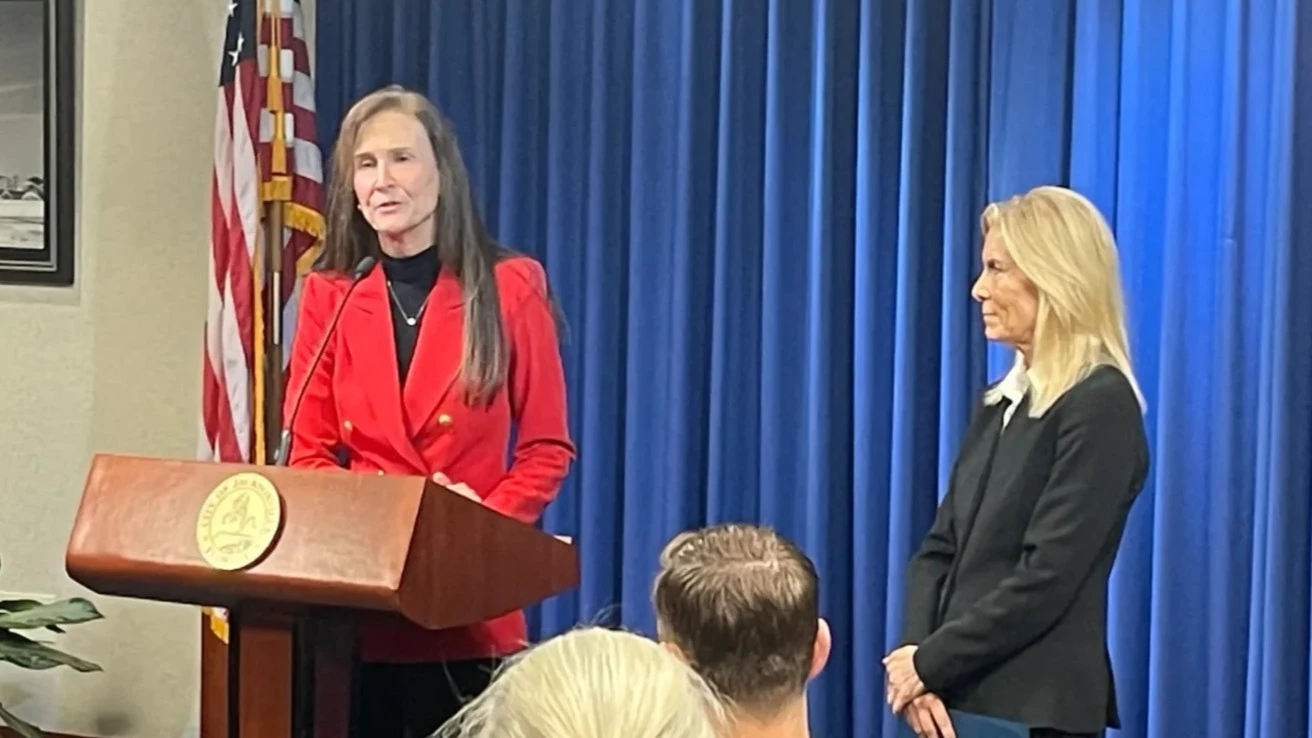 JEA CEO Vickie Cavey stands at a lectern in a red suit during a news conference. At her side is Jacksonville Mayor Donna Deegan.