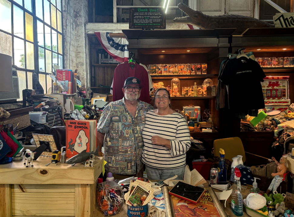 Eric (left) has a white beard and wears a black baseball hat and a grey and white patterned shirt. Christina (right) is wearing a black and white striped shirt. Both are smiling.