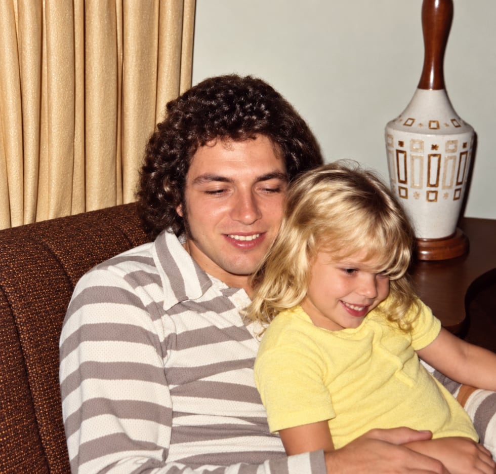 A young Gabrielle and Richard smile together on a chair.