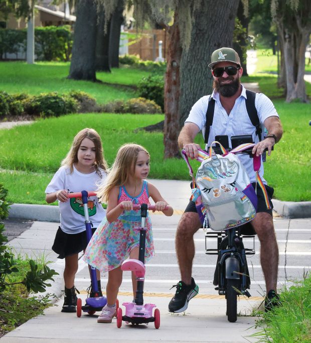Robert Borling and his two daughters, Kennedy, 7, and Vivian, 5, bike to Lake Silver Elementary School Friday, Sept. 11, 2026. Lake Silver is one of the almost 50 Orange County public schools operating at or below 65% capacity, according to OCPS enrollment data. (Joe Burbank/Orlando Sentinel)