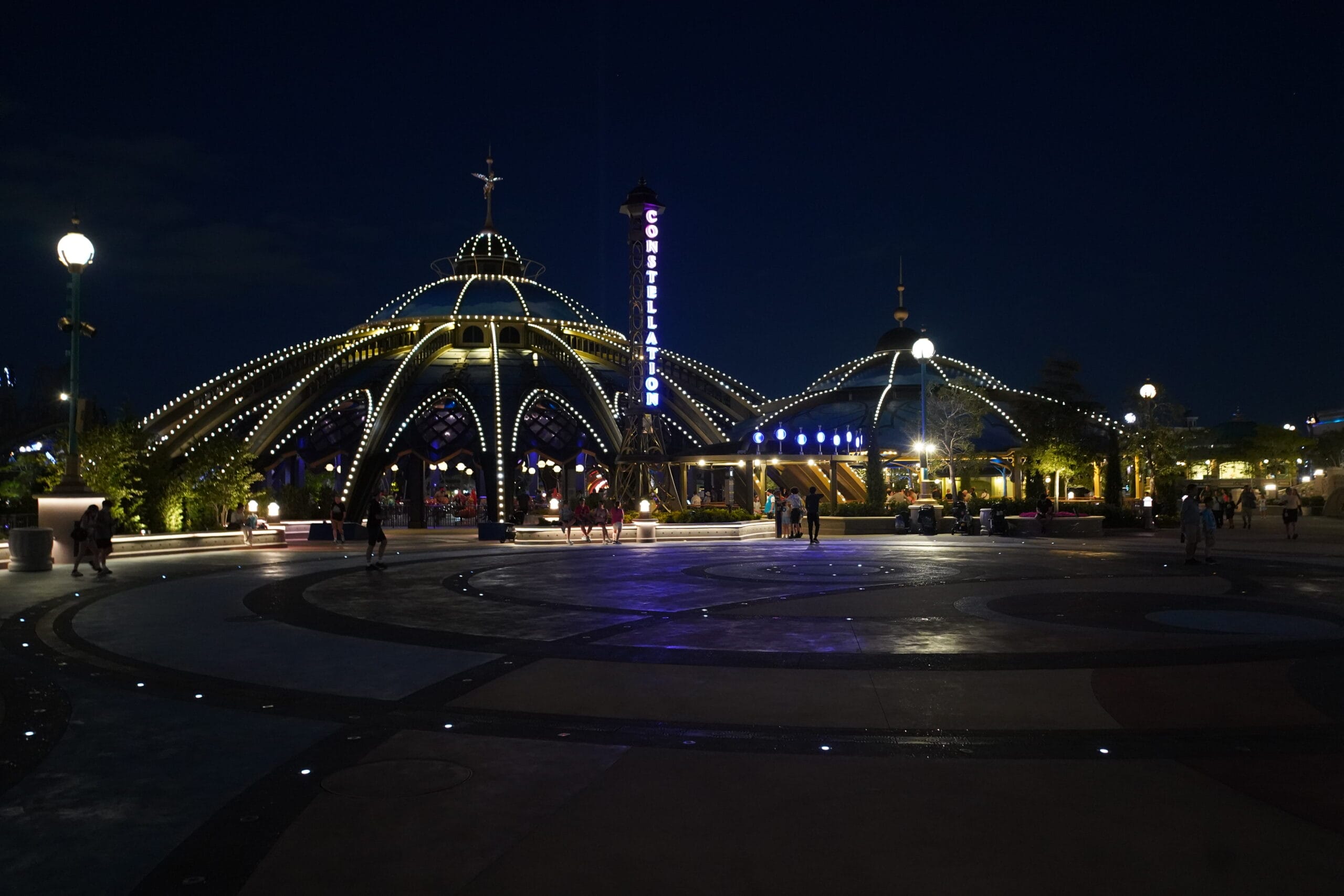 A dome-shaped pavilion with glowing lights at night, as people stroll the Universal Epic Universe plaza on the 4th of July.