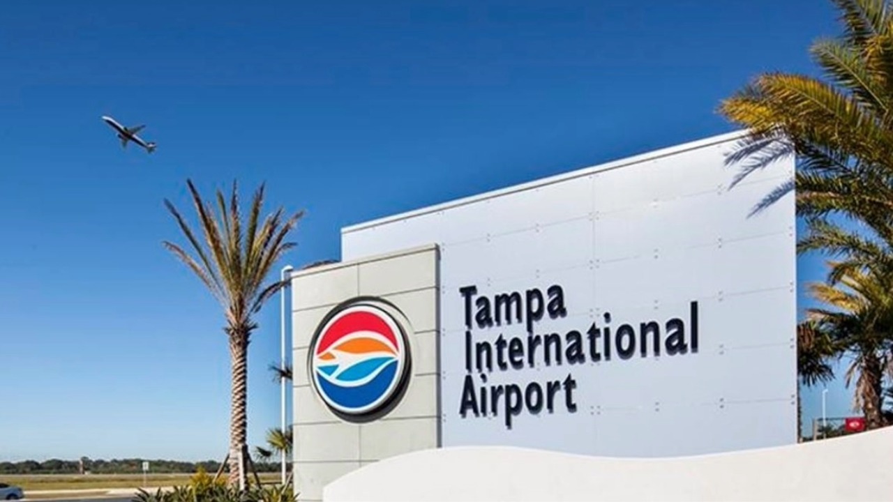 Sign for Tampa International Airport with airplane overhead and palm trees