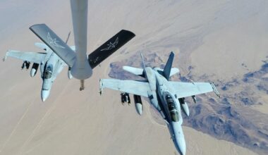 Two military aircraft fly alongside an aerial refueling tanker over a desert landscape.