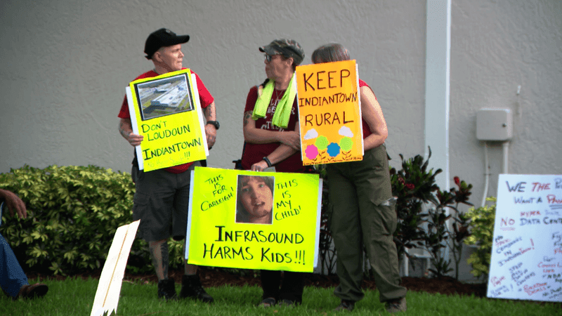 Residents hold signs calling for a pause on large-scale data center projects before a special Indiantown Village Council meeting Tuesday night. (WPEC)