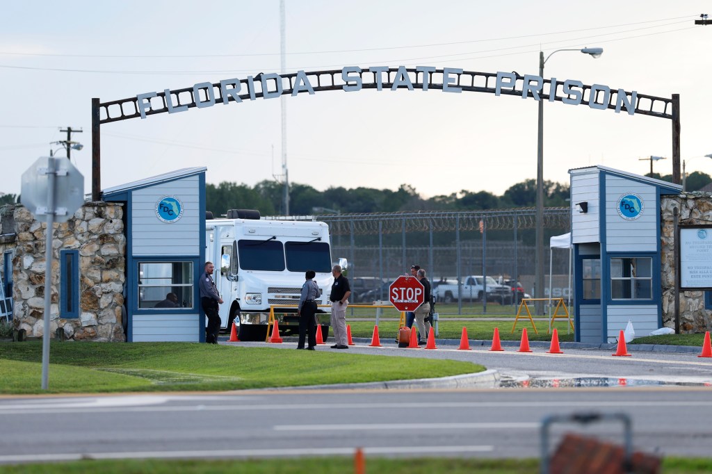 The entrance of Florida State Prison with a white armored truck, multiple security personnel, and a "STOP 100% ID CHECK" sign.