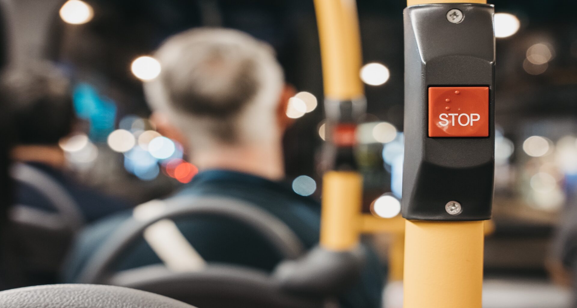 A bus stop button in a blurred interior bus setting with passengers in the background.