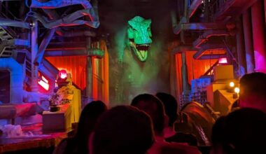 Guests on a Jurassic Park River Adventure raft approach the massive green-lit animatronic T. rex head inside the ride