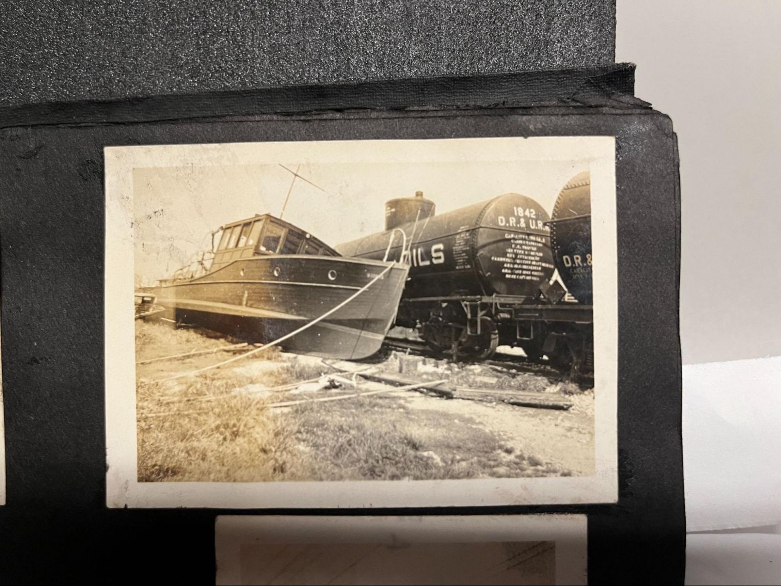Sepia photo of a boat on land leaning against a train.