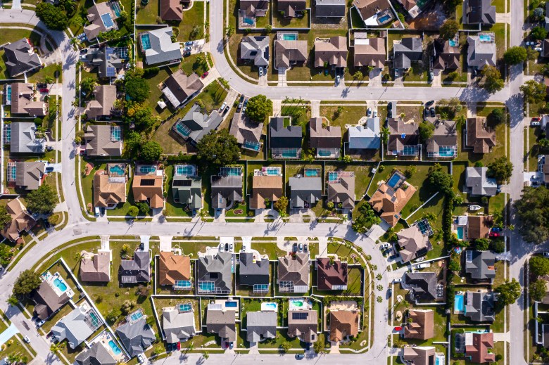 An aerial top-down photo shows a suburban residential neighborhood in Tampa, Florida, featuring single-family homes with private swimming pools, landscaped backyards, green lawns, and clean paved streets lined with palm trees.