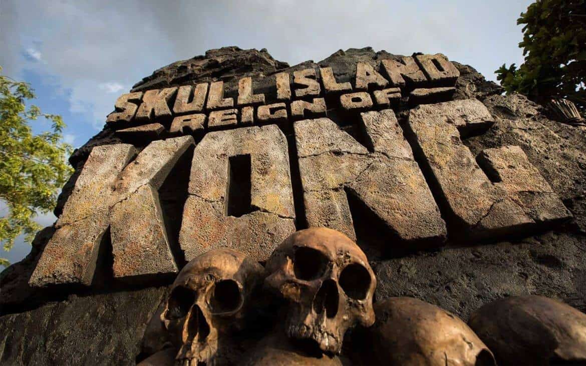 The towering stone entrance sign for Skull Island: Reign of Kong at Universal Orlando looms beneath a dramatic cloudy sky, with menacing skulls piled at its base, inviting guests to experience the thrilling adventure that awaits inside this legendary attraction.