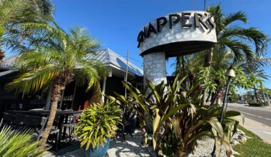 The outside seating area for Snappers Sea Grill, filled with tropical plants and palm trees under a clear blue sky.