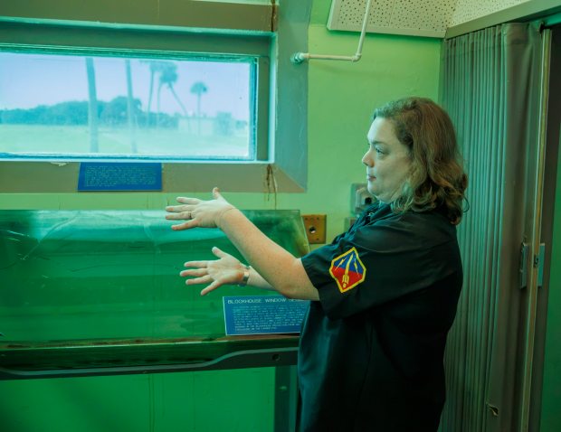 Sabra Gossett, a curator for the Cape Canaveral Space Force Museum, discusses early launch systems at Launch Complex 26 at the Cape Canaveral Space Force Museum during a visit on Aug. 12, 2026. Through the window is the launch pad used to send America's first satellite, Explorer 1, into space on Jan. 31, 1959. (Roger Simmons/Orlando Sentinel)